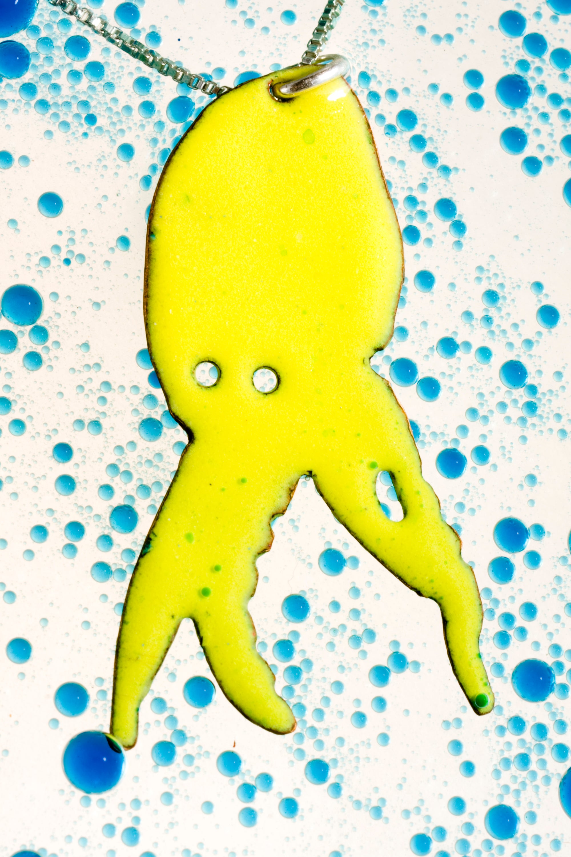 glass enamelled squid silhouette, profile of squid with cutout eyes, bright lime green vitreous glass enamel, fired to a high gloss finish, by peggy skemp 2008, sold at Wolfbait and B Girls, Chicago, IL. Photo with blue bubbles by AJ Kane.