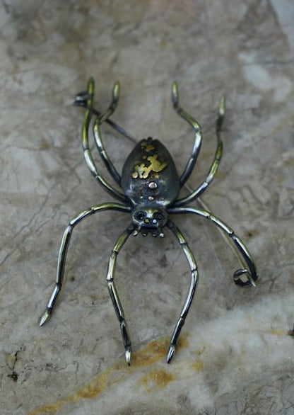 Large spider brooch by Peggy Skemp with fibula pin. Spider has white yellow and rose gold adornments on its back, hand engraved texture and 4 black diamond eyes, hand engraved legs.