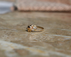 14k rose gold shell treasure ring with 3 diamonds, photo on a pink marble slab. The rose gold ring has a 1.5mm hammered band and 3 diamonds set with rustic beads to the side of the golden shell. By Peggy Skemp 2021